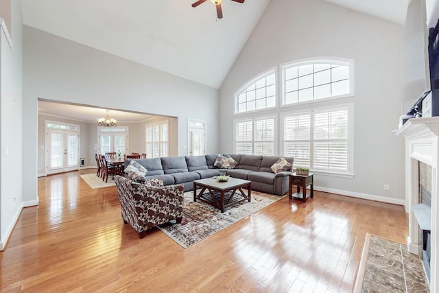 living room with ceiling fan with notable chandelier, light hardwood / wood-style floors, a fireplace, and high vaulted ceiling