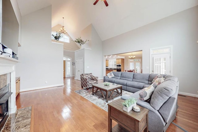 living room featuring a tiled fireplace, high vaulted ceiling, wood-type flooring, and ceiling fan with notable chandelier