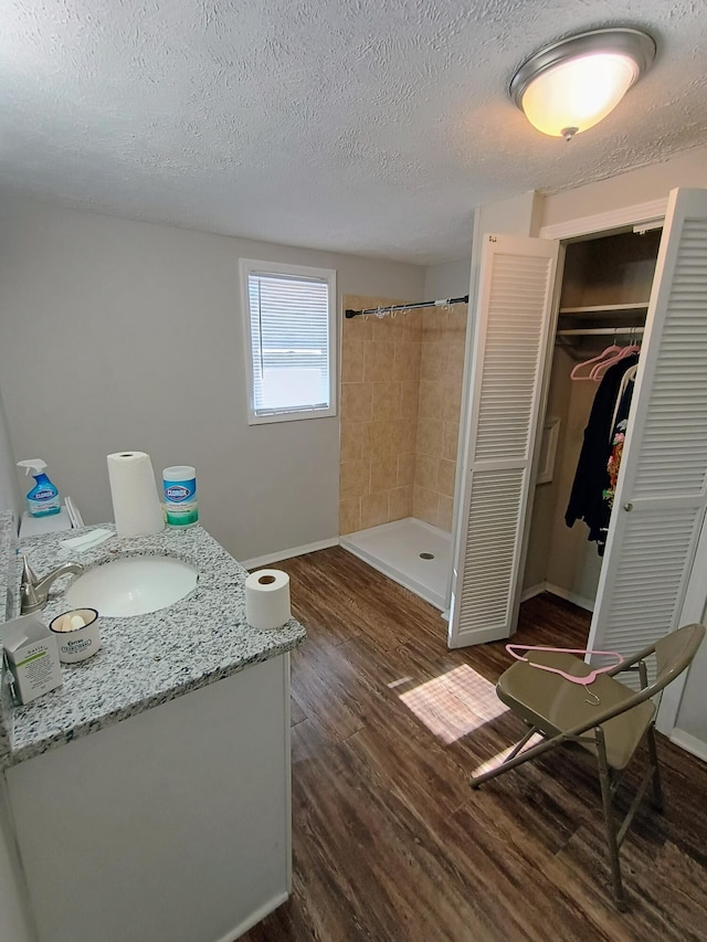 bathroom with a shower stall, baseboards, vanity, wood finished floors, and a textured ceiling