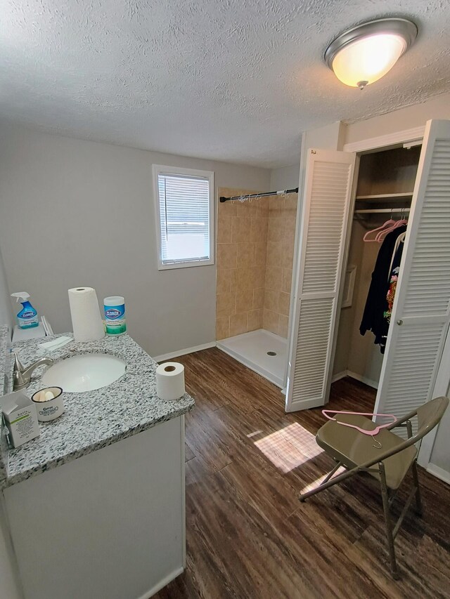 bathroom featuring a textured ceiling, wood finished floors, a shower stall, baseboards, and vanity