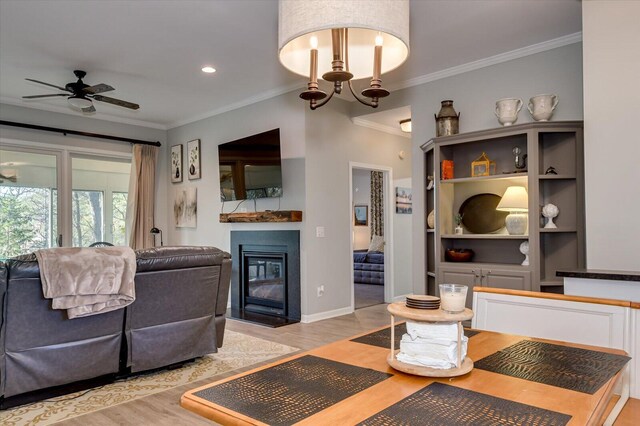 living room with ceiling fan with notable chandelier, light wood-type flooring, and crown molding