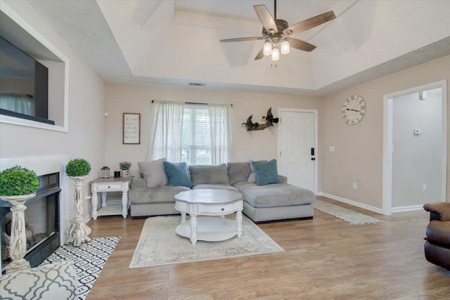 living room with a tray ceiling, ceiling fan, and light hardwood / wood-style floors