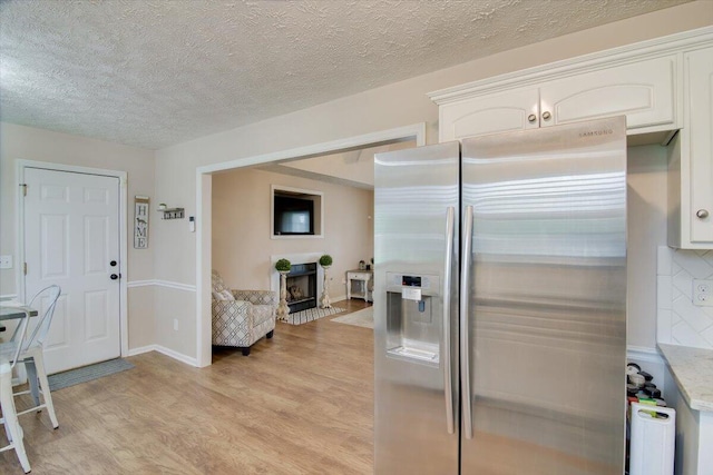 kitchen featuring white cabinets, stainless steel refrigerator with ice dispenser, light hardwood / wood-style flooring, decorative backsplash, and a fireplace