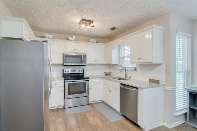 kitchen with light stone countertops, appliances with stainless steel finishes, sink, light hardwood / wood-style floors, and white cabinetry