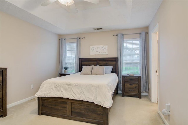 carpeted bedroom with multiple windows, a raised ceiling, and ceiling fan