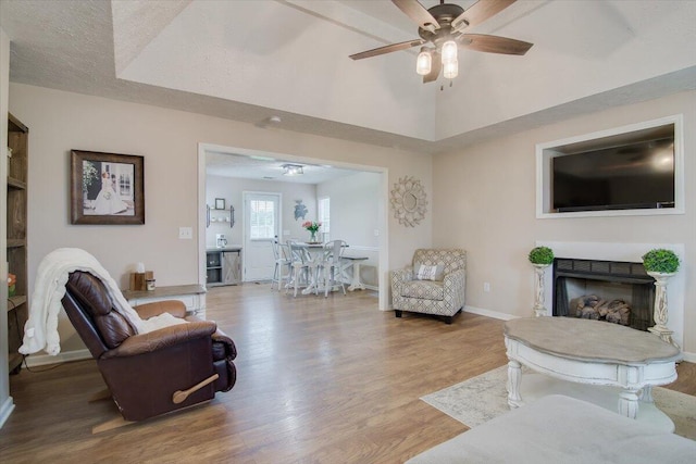 living room featuring a raised ceiling, ceiling fan, and light hardwood / wood-style flooring