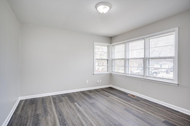 spare room featuring visible vents, baseboards, and dark wood-style flooring