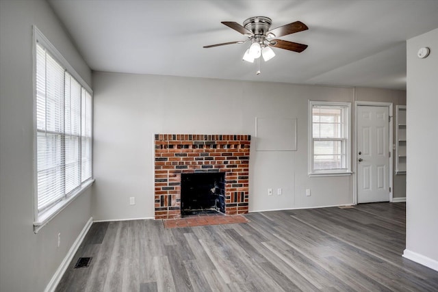 unfurnished living room with a fireplace, wood finished floors, a ceiling fan, and visible vents