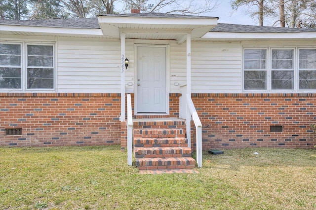 entrance to property featuring a lawn, brick siding, and crawl space