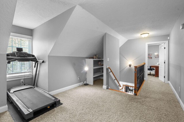 exercise area featuring carpet, a textured ceiling, and vaulted ceiling