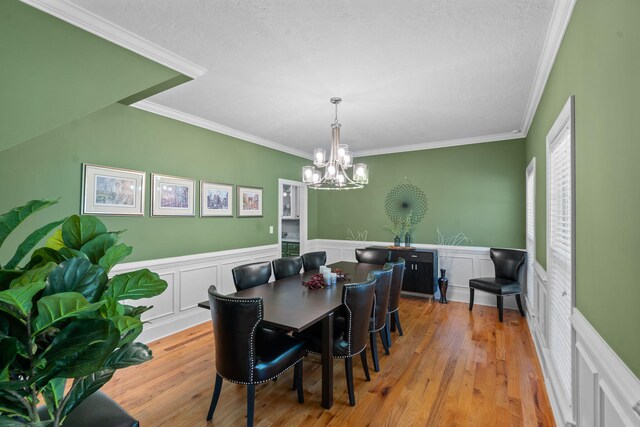 dining area with a textured ceiling, light hardwood / wood-style flooring, an inviting chandelier, and ornamental molding