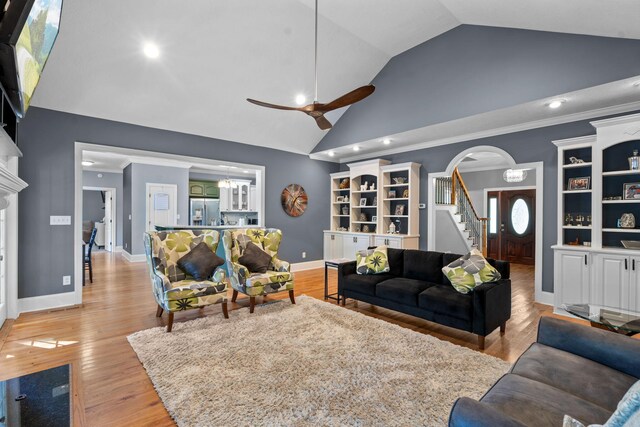 living room with ceiling fan with notable chandelier, light wood-type flooring, a fireplace, and lofted ceiling