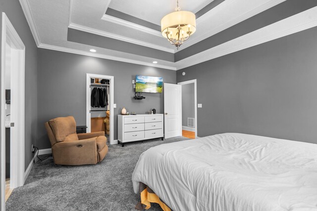 bedroom with an inviting chandelier, a walk in closet, crown molding, and a tray ceiling