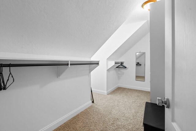 walk in closet with light colored carpet and lofted ceiling