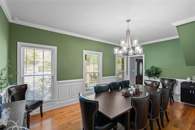 dining area with a notable chandelier, a healthy amount of sunlight, wood-type flooring, and crown molding