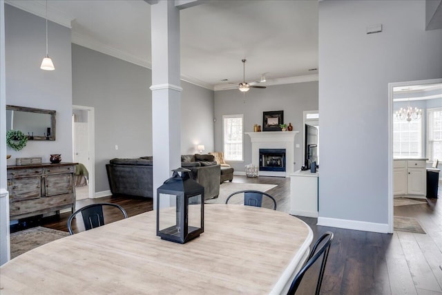 dining area featuring crown molding, ceiling fan, a fireplace, wood finished floors, and ornate columns