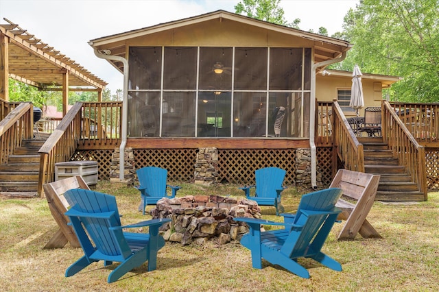 back of property with a sunroom, an outdoor fire pit, stairway, and a deck