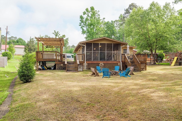 back of house with a wooden deck, a sunroom, an outdoor fire pit, a yard, and stairs