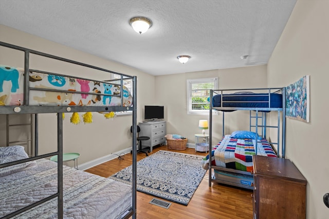 bedroom with a textured ceiling, baseboards, wood finished floors, and visible vents