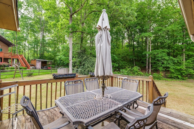 wooden terrace featuring fence, a storage unit, an outbuilding, outdoor dining area, and a lawn