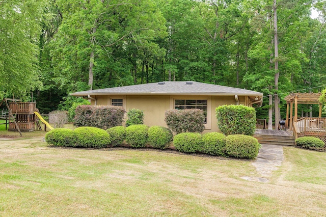 view of property exterior featuring a wooden deck, stucco siding, a playground, a yard, and a forest view