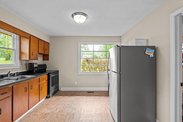 kitchen with brown cabinetry, dark countertops, baseboards, a sink, and appliances with stainless steel finishes