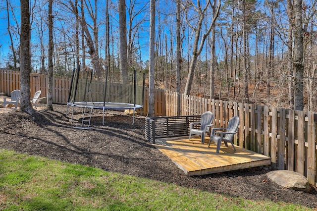 view of yard with a wooden deck, a trampoline, and a fenced backyard