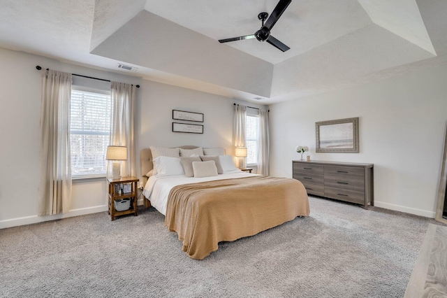 bedroom with visible vents, baseboards, carpet floors, multiple windows, and a raised ceiling