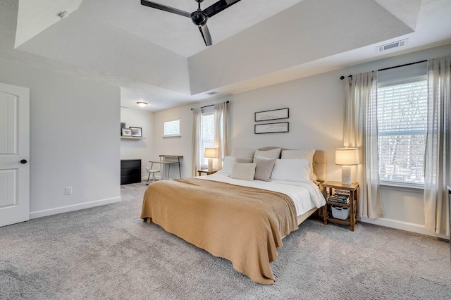 carpeted bedroom with multiple windows, a raised ceiling, and baseboards