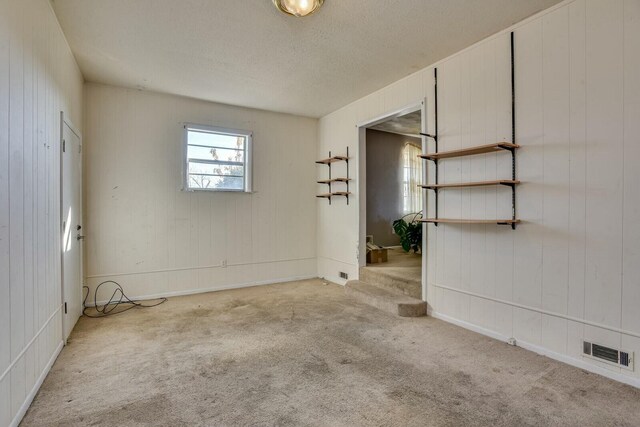 unfurnished room with wood walls, light colored carpet, and a textured ceiling