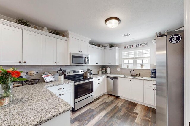 kitchen featuring dark wood-style flooring, appliances with stainless steel finishes, a sink, white cabinetry, and visible vents