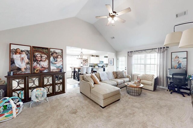 carpeted living room with high vaulted ceiling, ceiling fan with notable chandelier, and visible vents