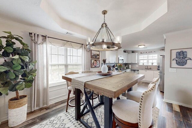 dining space featuring a tray ceiling, a notable chandelier, ornamental molding, and wood finished floors