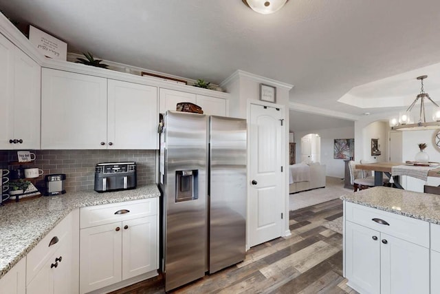 kitchen with white cabinets, arched walkways, stainless steel fridge, and light wood-style flooring