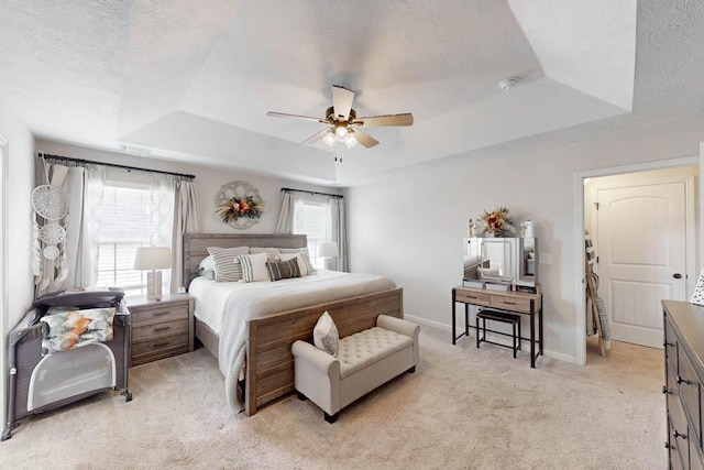 bedroom with a textured ceiling, a tray ceiling, light colored carpet, and baseboards