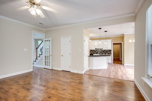 5107 Windmill Pl, Evans, GA 30809 - unfurnished living room with wood finished floors, crown molding, stairway, ceiling fan, and a chandelier