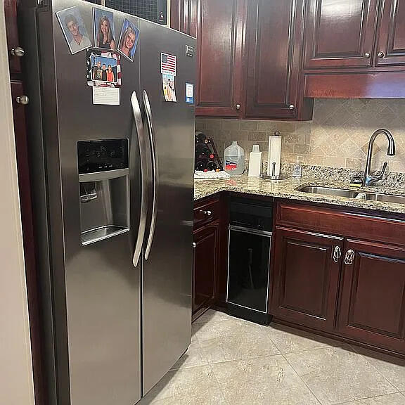 kitchen featuring sink, stainless steel refrigerator with ice dispenser, light stone countertops, tasteful backsplash, and light tile patterned flooring