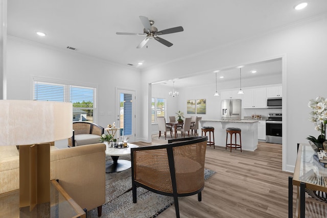 living room with ceiling fan with notable chandelier, light wood-type flooring, and ornamental molding