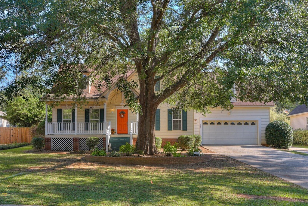 view of property hidden behind natural elements with a front lawn, a porch, and a garage