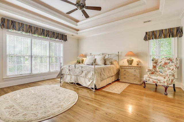 bedroom with multiple windows, hardwood / wood-style flooring, and a tray ceiling