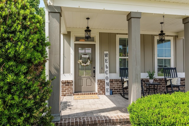 doorway to property with covered porch, board and batten siding, and brick siding