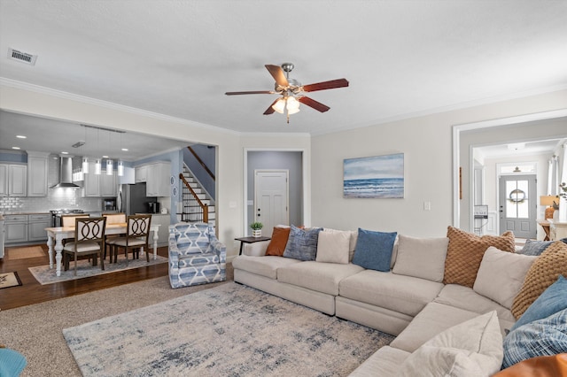 living room with ceiling fan, stairway, ornamental molding, and wood finished floors