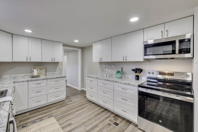 kitchen with white cabinets, light wood-type flooring, stainless steel appliances, and light stone countertops