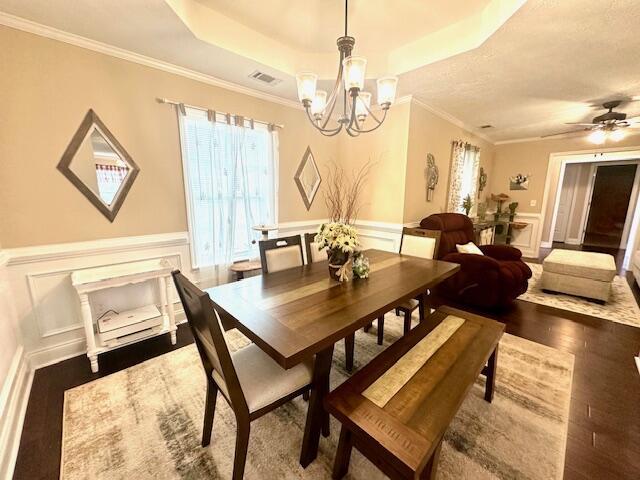 dining space featuring a tray ceiling, ornamental molding, ceiling fan with notable chandelier, and hardwood / wood-style flooring