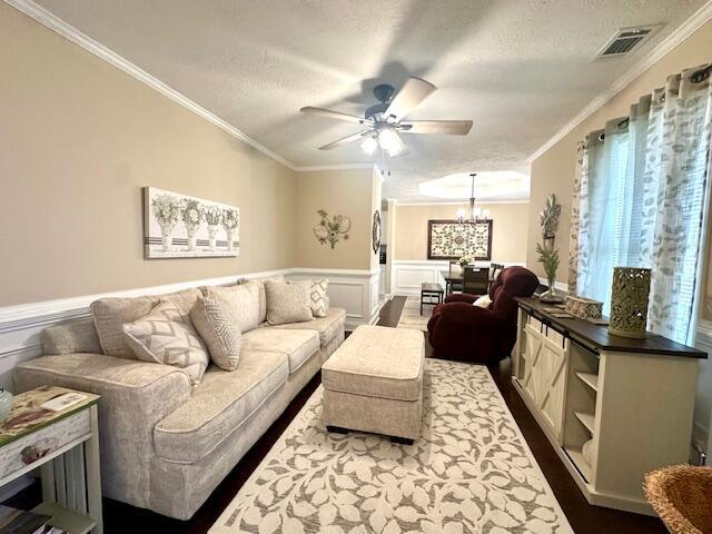 living room with ceiling fan with notable chandelier, a textured ceiling, dark hardwood / wood-style floors, and crown molding