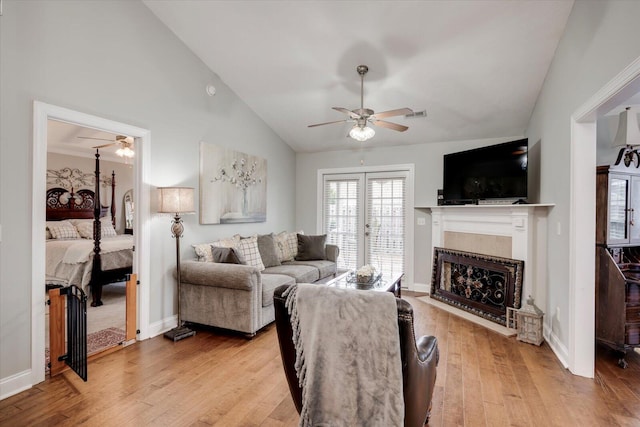 living room featuring lofted ceiling, a fireplace with flush hearth, ceiling fan, light wood-type flooring, and baseboards