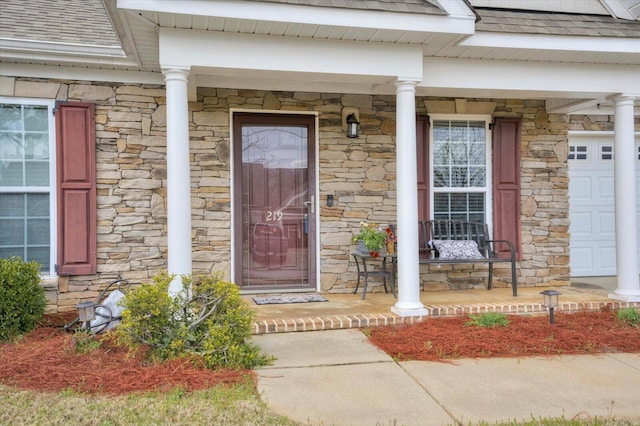 property entrance with a garage, stone siding, covered porch, and roof with shingles