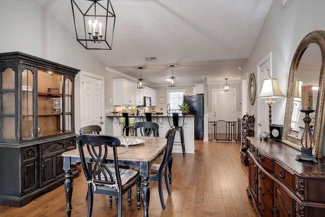 dining space with wood-type flooring, visible vents, a notable chandelier, and ornamental molding