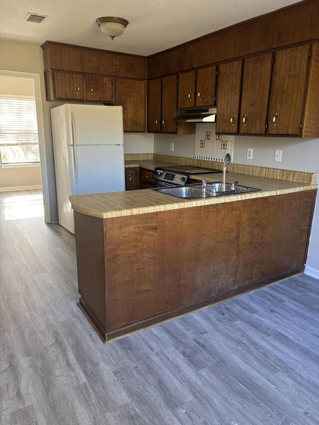 kitchen featuring sink, light hardwood / wood-style flooring, kitchen peninsula, white fridge, and a textured ceiling