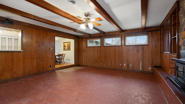 empty room featuring visible vents, a ceiling fan, brick floor, wood walls, and beam ceiling